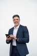 © Stock 4 You - Mature businessman in suit holding cellphone isolated, white background. Smiling Latin business man using smartphone mobile phone screen device, scrolling app, working and looking at camera. Vertical
