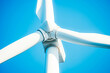 © VisualProduction - A close-up of a wind turbine with giant white blades spinning against a clear blue sky.
