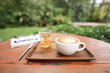 White coffee cup and bael tea on brown wooden table with green lush background