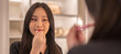 Smiling beautiful asian woman fresh healthy skin looking on mirror and enjoying applying skincare lips with red lipstick at home.facial beauty and cosmetic concept