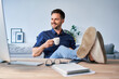 Relaxed businessman having break drinking coffee sitting with feet up on the desk looking at computer