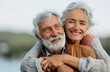 © RumRaisinStock - An elderly man and woman are holding each other tightly in a warm embrace, showcasing their strong bond and affection towards one another. The couples faces are filled with joy and love.
