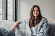 © Daniel - Happy attractive young adult woman girl sitting on sofa looking at camera in modern cozy home, smiling single 20s lady beautiful face relaxing on couch alone enjoy wellbeing posing for portrait.