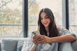 © Daniel - Happy pleasant millennial woman relaxing on comfortable couch, holding smartphone in hands. Smiling young lady chatting in social networks, watching funny videos, using mobile applications at home..