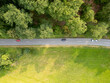 Top down view of three cars on the country road between the trees and the field