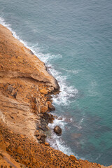 waves hitting against the cliffs on the outskirts of Benidorm, Image shows a dark cloudy day with a steep cliff face and the warm Mediterranean waves crashing against the bottom of the cliff 