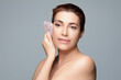 Woman using a gua sha stone for facial massage against a calm background