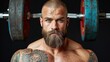 © K-MookPan - A muscular man with a beard and tattoos is standing in front of a barbell. He is looking at the camera with a determined expression. The background is black.