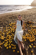 beautiful woman with dark hair in elegant white dress posing on the Cyprus beach with a lot of lemons