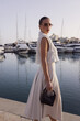 beautiful woman with dark hair in elegant classic clothes with accessories posing at the marina with the yachts in Cyprus