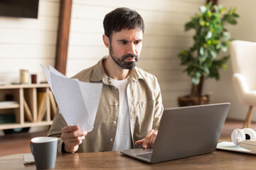 Aufkleber - Distressed man is sitting at a table with a laptop open in front of him, surrounded by papers. He appears focused and engaged in his work, typing and reviewing documents.