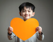 Small Asian boy holding empty orange paper heart in front of him. Generative AI	