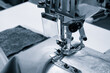 A sewing machine is in use, with a piece of fabric being sewn. The machine is black and silver, and the fabric is white. Scene is focused and precise
