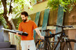 Image showing healthy athletic caucasian man holding his toolbox in home yard for bicycle maintenance. Sports-loving active male cyclist exploring professional equipments outside.
