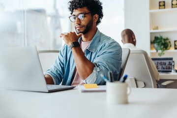 Focused young man working at laptop in bright office