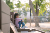Fototapeta  - A little girl sits on a bench in a park