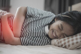 Fototapeta  - A girl is laying on a bed with a stomach ache