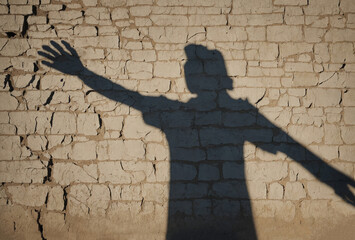 Shadow of a man on white brick wall and wooden floor, Abstract image of  european businessman with lifted up hands , shadow on brick wall background. Confidence and strength concept
