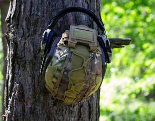 Wall Mural - A tactical helmet and active tactical headphones hang on a tree branch. Defense of the military, military operations. War in Ukraine