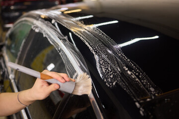 Wall Mural - A person is cleaning a car windshield with a brush and water