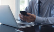 © tippapatt - Businessman using mobile phone searching the information and working on laptop computer at office. Business man online working and using smartphone surfing the internet, business concept