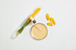 A round petri dish with yellow liquid extract from sunflower and a serum bottle in above next to a test tube containing some sunflower petals and green leaves. Blank space for design, top view
