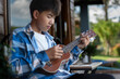 © Sophon_Nawit - Asian preteen boy playing ukulele and acoustic guitar at home, lifestyle and hobby of children concept.