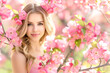 A woman with blonde hair is standing in front of a tree with pink flowers