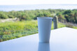 A blank white disposable paper cup is placed on the table, with a blurry view of green bushes in the background. The concept of sustainable living and environmental awareness