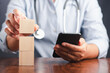 Close-up of doctor's hands holding a smartphone and wooden cube on a wooden table.