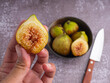 Close-up of hand holding a fig with figs in a bowl on a table.