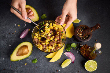 Wall Mural - Woman mixing chopped tuna, mango, cilantro and onion in a glass bowl cooking traditional tuna and mango tartare