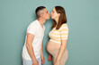Loving Caucasian young married pregnant family standing isolated over light green background expecting parents kissing expressing love and tenderness