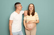Laughing positive cheerful pregnant Caucasian young couple standing isolated over light green background future parents expressing happiness laughing happily