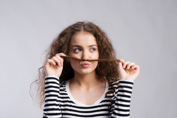 Sticker - Portrait of a gorgeous teenage girl with curly hair, holding lock of hair as a moustache. Studio shot, white background with copy space