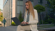Pensive Caucasian woman businesswoman student female business lady girl developer think typing on laptop outdoors street near office work remote online thinking pondering idea journalist write article