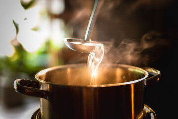 Wall Mural - A boiling pot steams up as a restaurant's chef uses a ladle to stir soup in a cooking pot in the morning.