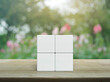 Four white block cubes on wooden table over blur pink flower and tree in garden