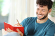 Happy man writing in agenda sitting at home