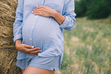 Wall Mural - Pregnant woman holds hands on belly on nature background, outdoors.