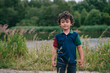 Adorable young boy with curly hair enjoying a serene walk near a lake, surrounded by lush greenery and wildflowers