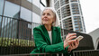 © Halfpoint - Mature businesswoman holding smartphone, waiting for business partner in the city. Beautiful older woman with gray hair standing on city street.