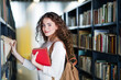 © Halfpoint - Young female student in library, looking for books, preparing for final exam.