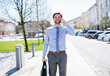 Handsome businessman phone calling on smartphone, standing in city street. Working remotely, waiting for business meeting. Manager smiling, outdoor in urban setting