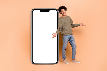 Poster - Full body photo of young guy wear sweatshirt demonstrate shrug shoulders big display phone touchscreen application isolated on beige color background