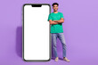 © deagreez - Full body photo of young happy man wear green t-shirt folded arms near smartphone screen ad web eshop isolated on purple color background