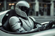 A man in a white knight suit and helmet sits in a sleek silver car. The modern setting contrasts with his medieval knightly attire