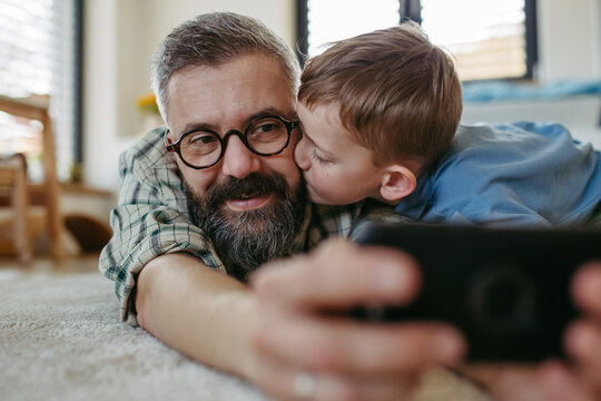 little boy making selfie on smartphone with father, lying on floor in kids room, making silly faces.