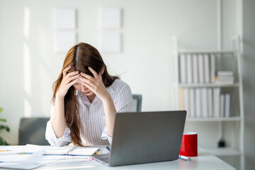 Wall Mural - A woman is sitting at a desk with a laptop and a red cup. She is looking at the laptop with a worried expression on her face