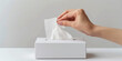 © Nano Photos - A person's hand is pulling a tissue from a white rectangular box on a plain surface against a neutral background.